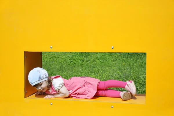 Feliz niña linda en caja amarilla con ventana en el patio de recreo a — Foto de Stock