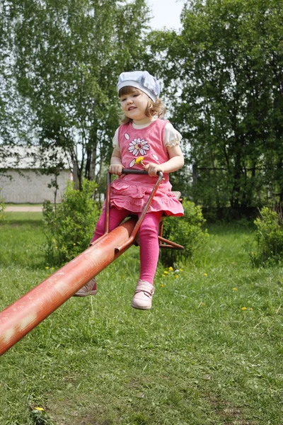 Happy little cute girl in pink rides on red seesaw at summer day — Stock Photo, Image