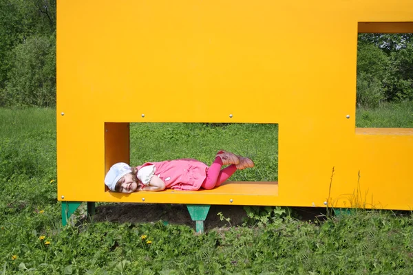Happy little cute girl lies in window of yellow box at playgroun — Stock Photo, Image