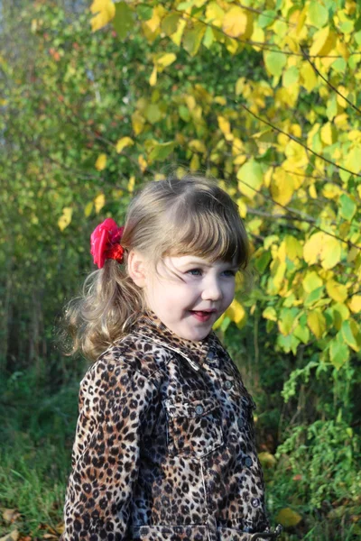 Smiling little girl looks away next to yellow trees in park at s — Stock Photo, Image