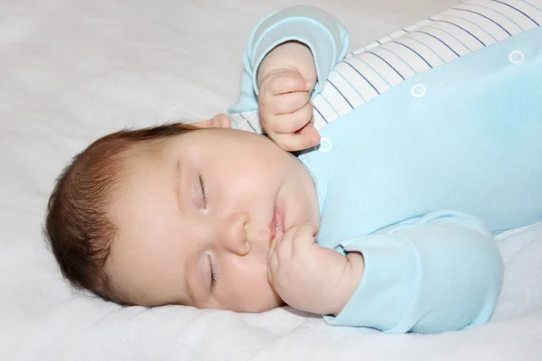Little beautiful baby in blue jumper sleeps on white sheet on be — Stock Photo, Image