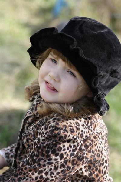 Beautiful happy little girl in black hat looks away outdoor at a — Stock Photo, Image