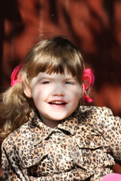 Pretty happy little girl with pink bows in overcoat smiles at su — Stock Photo, Image