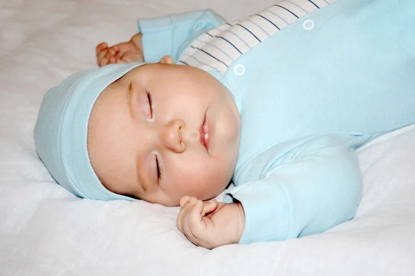 Piccolo bel bambino in maglione blu e cappello dorme su bianco lei — Foto Stock