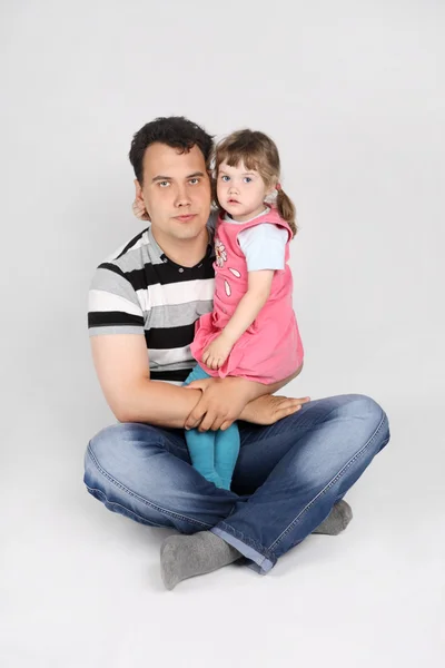父亲手上拿他的小女儿坐在地板上灰色的背景上 — 图库照片