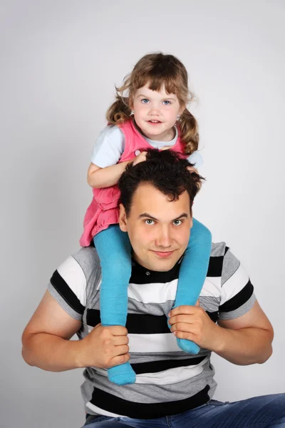 Llittle cute daughter sits on shoulders of his father on grey ba — Stock Photo, Image