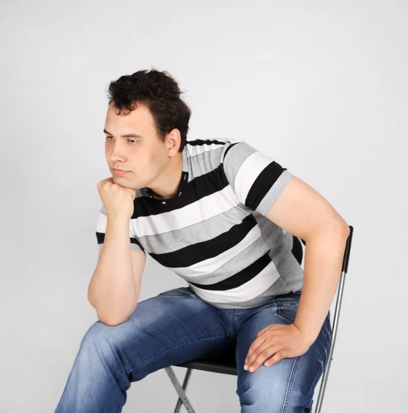 Brunet man in striped T-shirt sits on chair and thinks on grey b — Stock Photo, Image