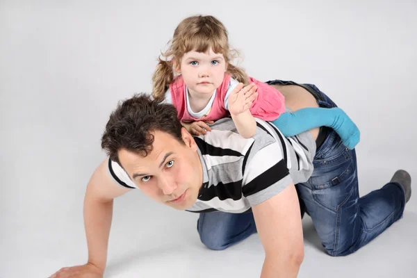 Llittle cute daughter lies on back of his father and waves hand — Stock Photo, Image