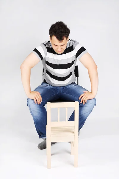 Brunet hombre guapo se sienta en la silla y se ve pequeña silla de madera o —  Fotos de Stock