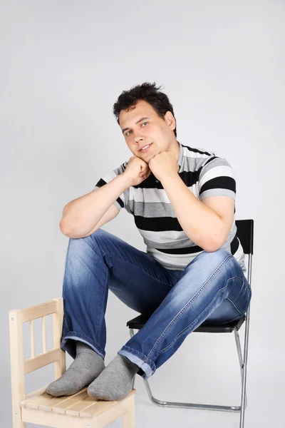 Smiling man sits on big chair and puts feet on small chair on gr — Stock Photo, Image