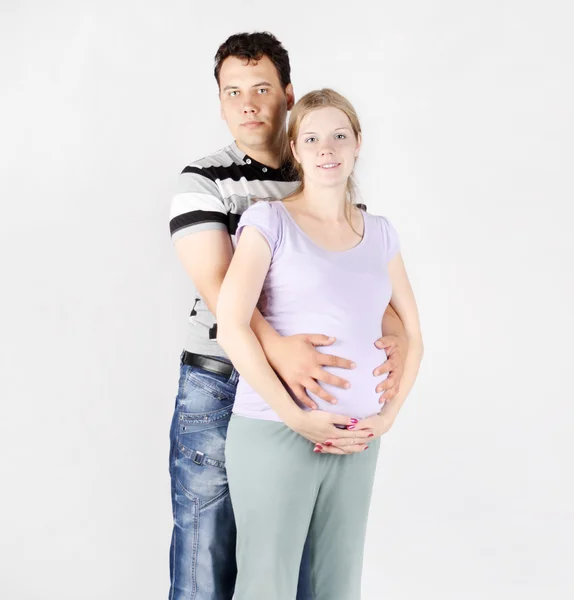 Hombre guapo abraza el vientre de la mujer embarazada sobre fondo gris . — Foto de Stock