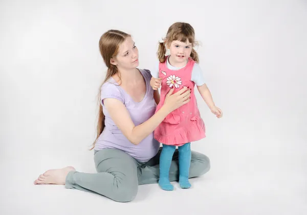 Pregnant woman sits on floor near little smiling daughter on gre — Stock Photo, Image