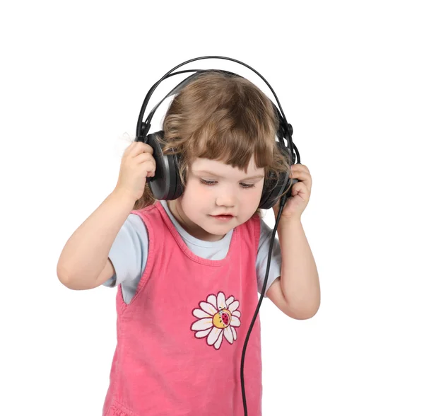 Little girl listens to music in big headphones and looks down is — Stock Photo, Image