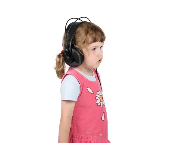 Little girl listens to music in big headphones and looks away is — Stock Photo, Image