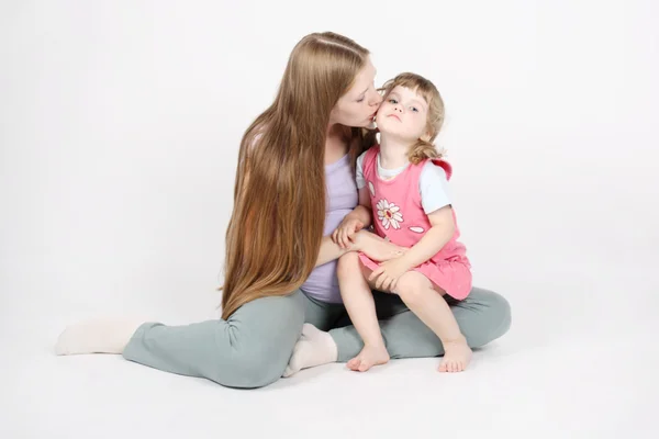 Pregnant woman sits on floor and kisses her little daughter on g — Stock Photo, Image