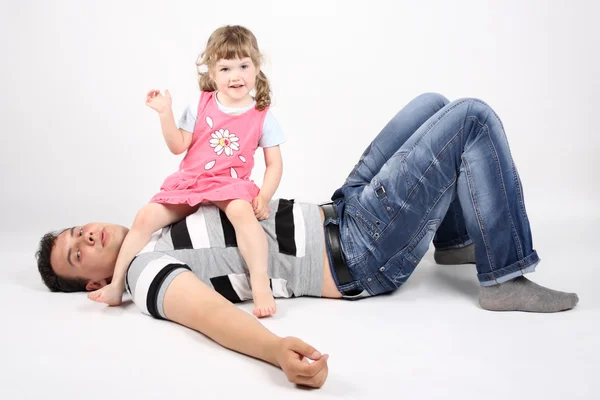 Felice padre si trova sul pavimento e piccola figlia felice si siede sul suo — Foto Stock