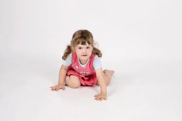 Little smiling barefoot girl in pink creeps on floor and looks a — Stock Photo, Image
