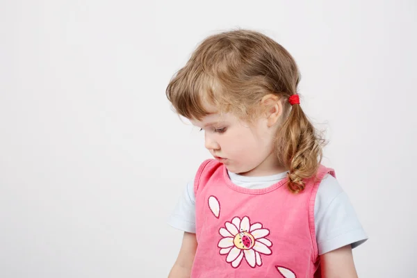 Little beautiful girl in pink looks down and thinks on white bac — Stock Photo, Image