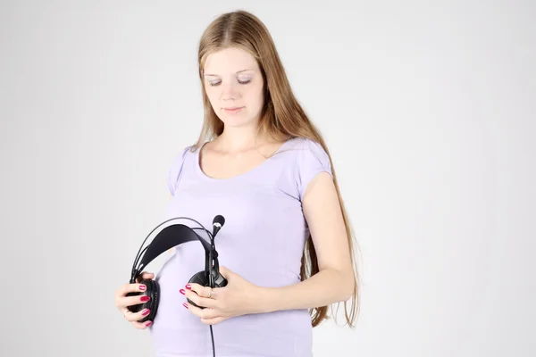 Pregnant beautiful woman put big black headphones to belly on gr — Stock Photo, Image
