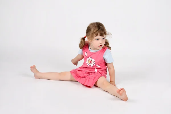 Little surprised barefoot girl in pink sits on floor and looks a — Stock Photo, Image
