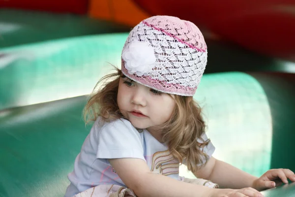 Little beautiful girl in openwork hat on green inflatable trampo — Stock Photo, Image