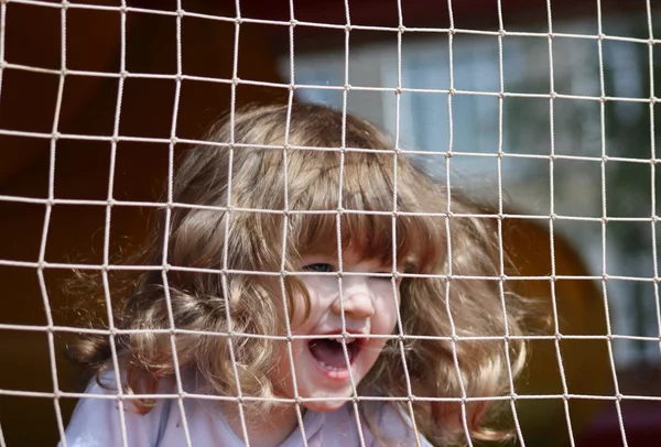 Pequena menina feliz bonita grita em playground verde com grade — Fotografia de Stock