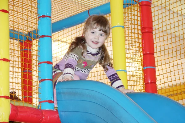 Маленька мила дівчинка на синьому пластиковому слайді на внутрішньому дитячому майданчику . — стокове фото