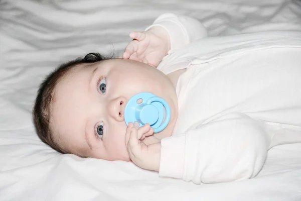 Little beautiful baby in light jumper lies on white sheet on bed — Stock Photo, Image