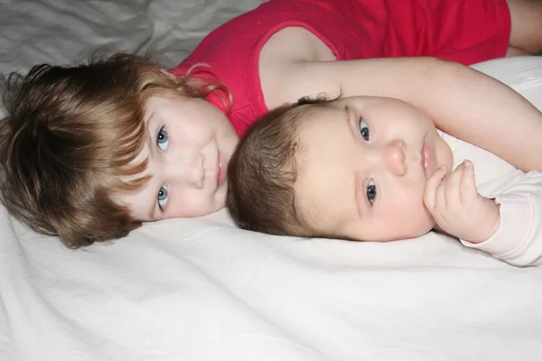 Pequeno bebê bonito e menina bonita encontra-se no lençol branco na cama — Fotografia de Stock