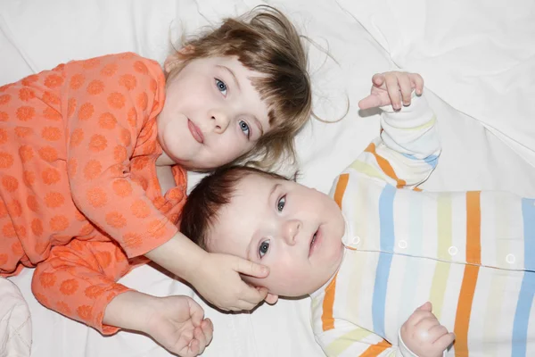 Petit frère et jolie soeur allongés sur un drap blanc sur le lit et l — Photo