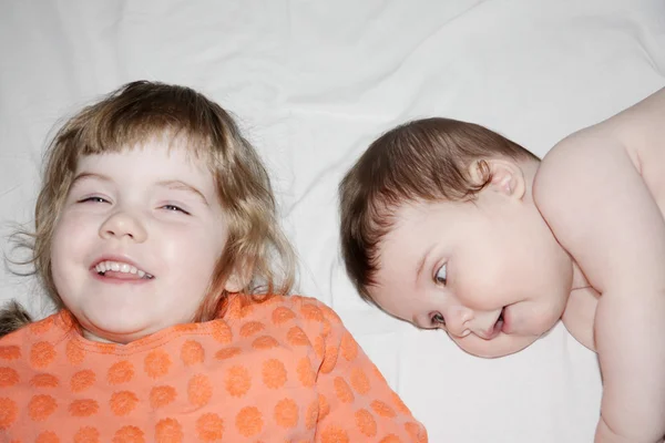 Little brother and pretty sister smile and lie on white sheet on — Stock Photo, Image