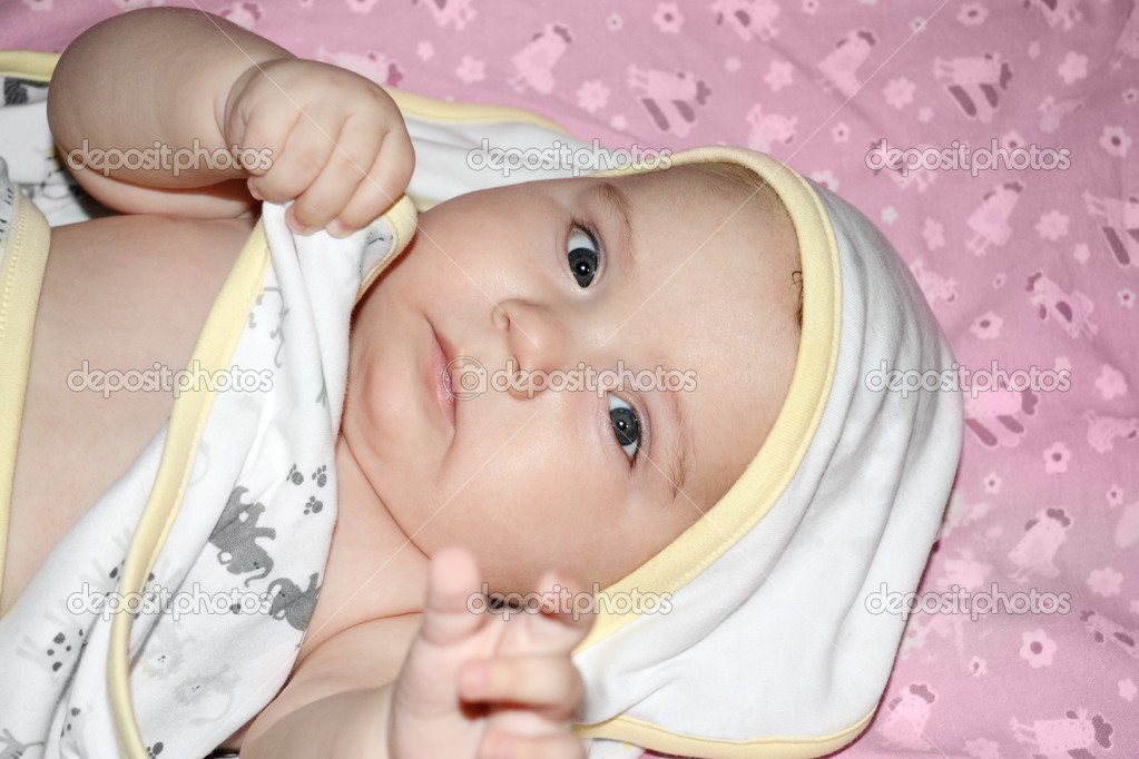 Little beautiful baby in towel lies on pink sheet on bed and loo