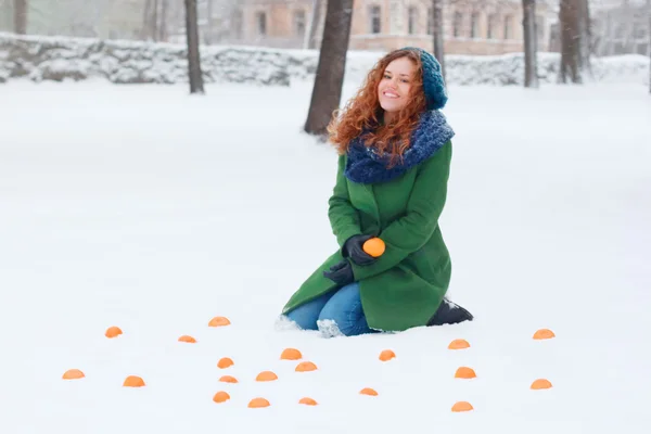 Beautiful girl sits in snow among mandarins at winter day in par — Stock Photo, Image