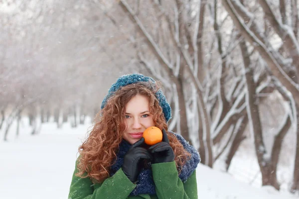 Beautiful girl holds mandarin and looks at camera at winter day — Stock Photo, Image