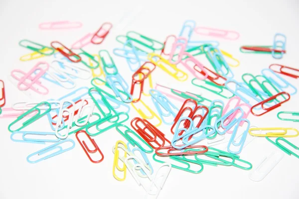 Pile of many multicolored plastic paper clips on white paper. — Stock Photo, Image