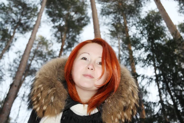 Happy redhead girl looks at camera in pine forest at winter. — Stock Photo, Image