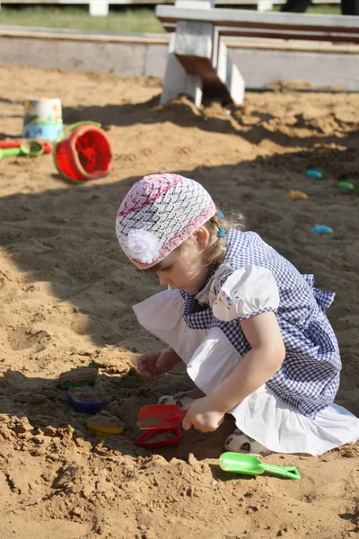 Little girl in dress plays in sandbox with shovel on summer day. — Stock Photo, Image
