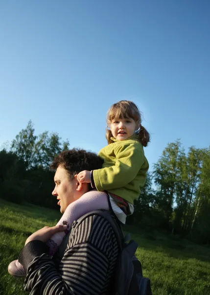 La piccola figlia felice si siede su spalle di suo padre all'aperto . — Foto Stock