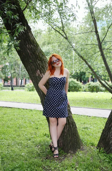 Beautiful girl stands near tree and smiles in park at summer day — Stock Photo, Image