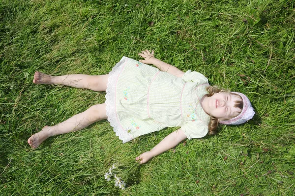Little barefoot girl lies on green grass of meadow at summer sun — Stock Photo, Image