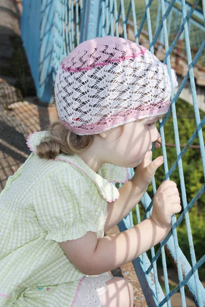 Little pretty girl looks through blue grid at summer sunny day — Stock Photo, Image