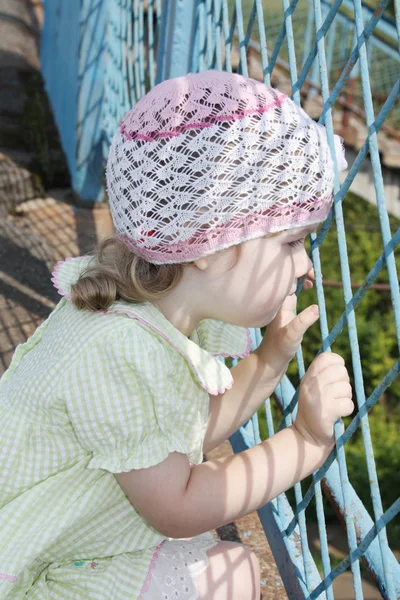 Kleines hübsches Mädchen blickt durch blaues Gitter an sonnigem Sommertag — Stockfoto