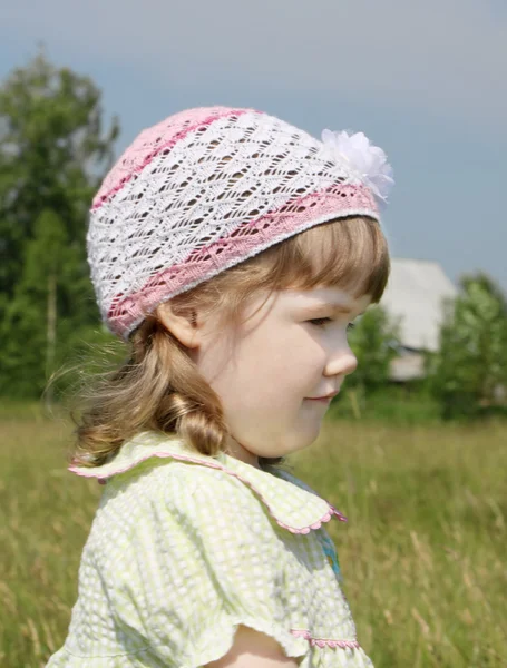 Smiling little girl looks away at meadow near village at summer — Stock Photo, Image