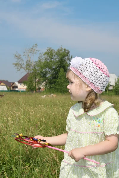 Petite fille avec moulin à vent regarde loin prairie près du village à s — Photo