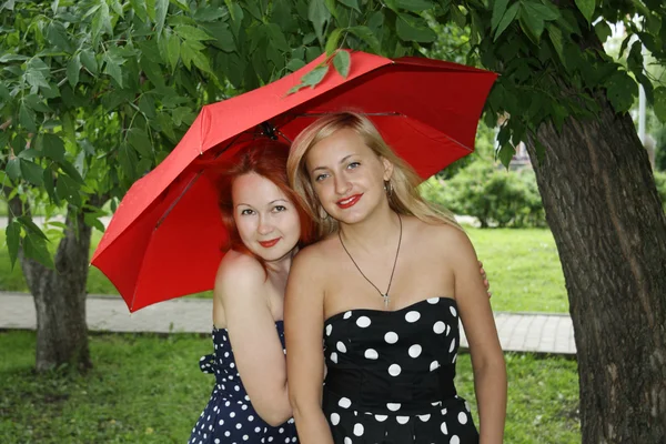 Two beautiful girls with red umbrella stand in park at summer da — Stock Photo, Image