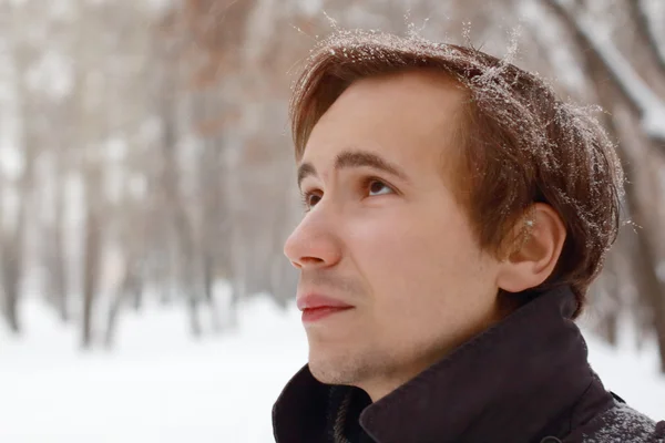 Jovem com flocos de neve no cabelo olha para cima ao ar livre no inverno sno — Fotografia de Stock