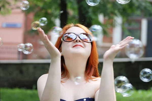 Pretty smiling girl in sunglasses catches soap bubbles in park a — Stock Photo, Image