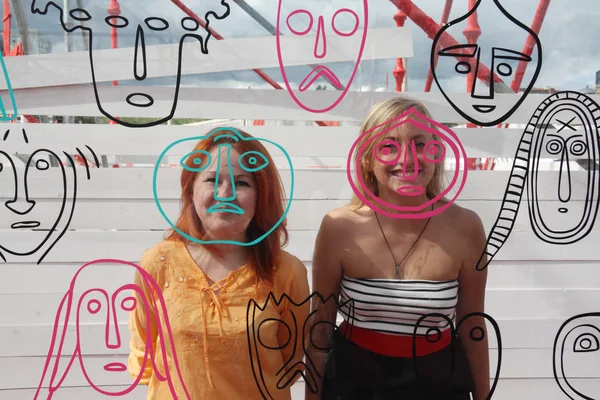 Duas meninas felizes sorriem atrás da parede de vidro com rostos no dia de verão — Fotografia de Stock