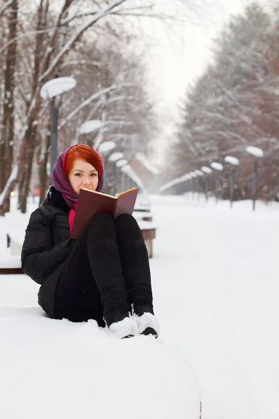 Bella ragazza in nero si siede sulla panchina con libro all'aperto a winte — Foto Stock