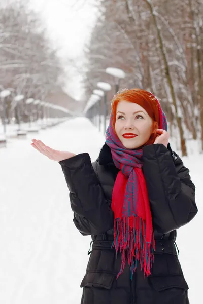 Bella ragazza felice in fazzoletto rosso cattura fiocchi di neve all'aperto a — Foto Stock